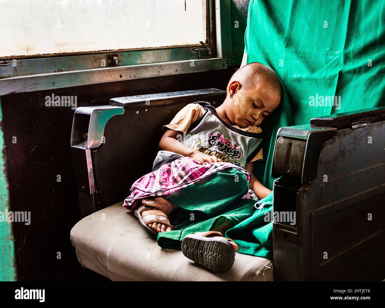 Mandalay, MYANMAR - 14 AVRIL 2017: Corps complet de la petite fille bald asiatique mignonne en vêtements décontractés assis et dormant sur un siège sale de merde dans le vieux train Banque D'Images