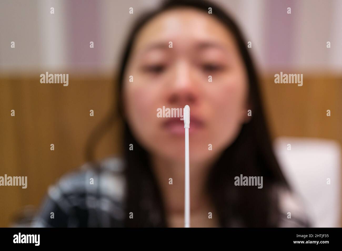 Jeune femme asiatique avec écouvillon nasal en coton faisant un test d'expression d'antigène dans la chambre d'hôtel légère pendant la quarantaine et la pandémie de coronavirus Banque D'Images