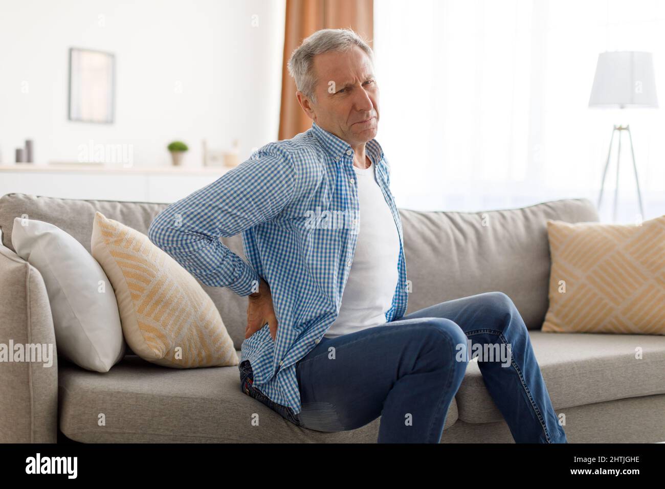 Homme mature avec douleur dorsale assis sur le canapé à la maison Banque D'Images