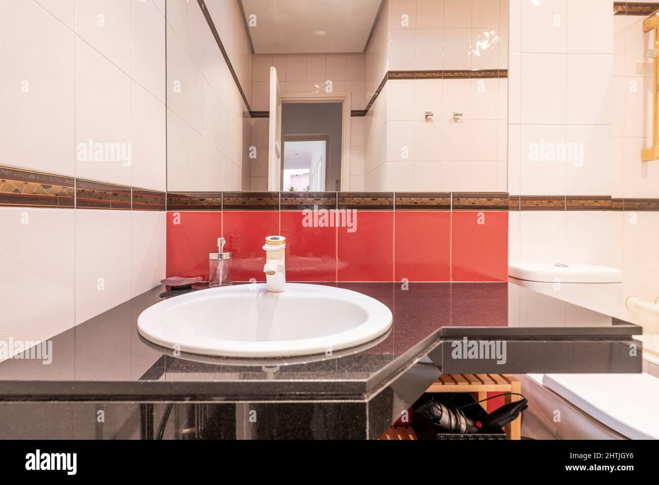 Salle de bains avec meuble-lavabo en marbre noir et évier en porcelaine blanche avec miroir en verre sans cadre carré, carrelage rouge et blanc et toilettes en porcelaine Banque D'Images