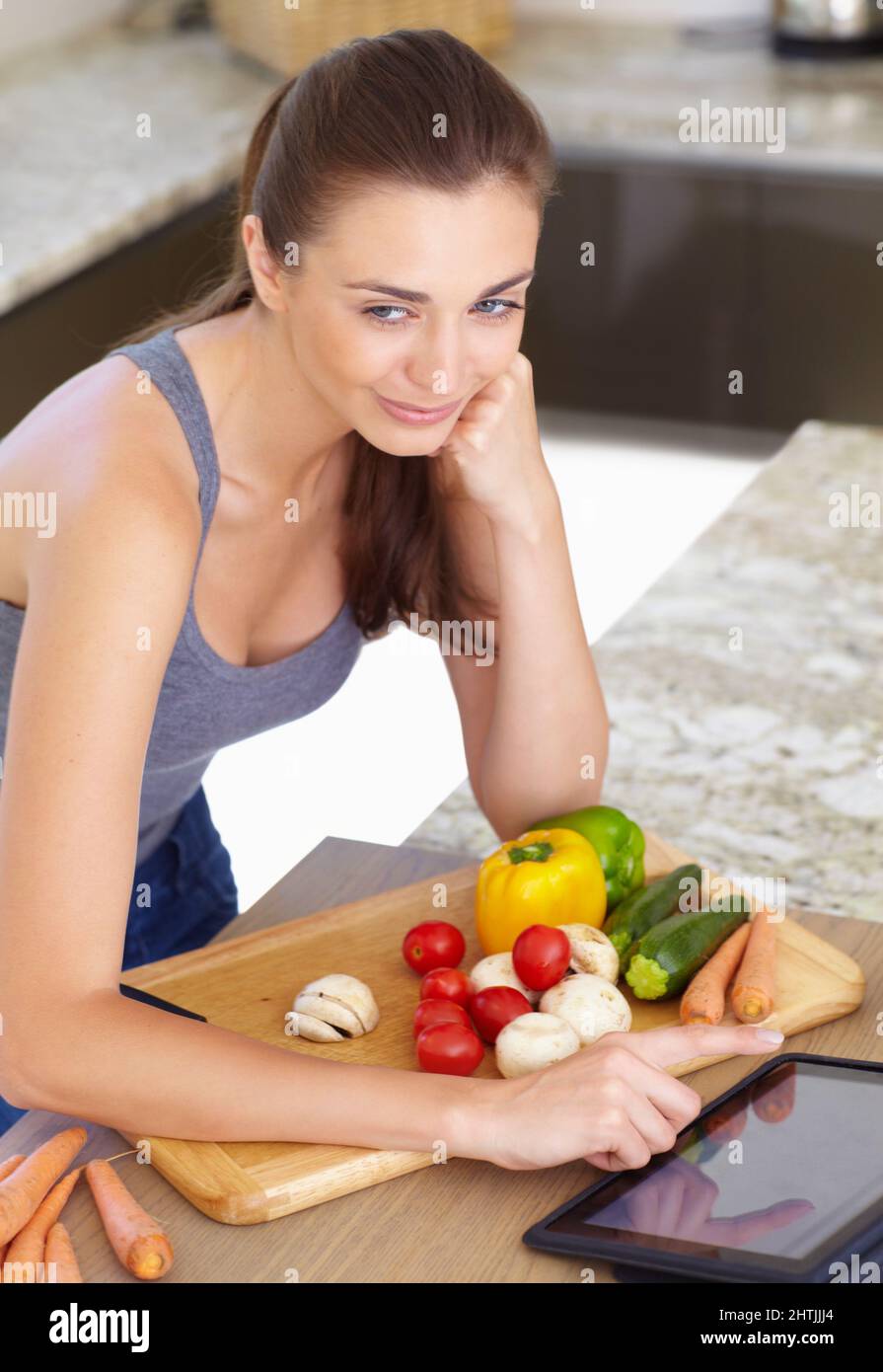 Une recette en ligne pourrait être bonne Une jeune femme attirante à la recherche de recettes sur sa tablette numérique tout en cuisinant. Banque D'Images