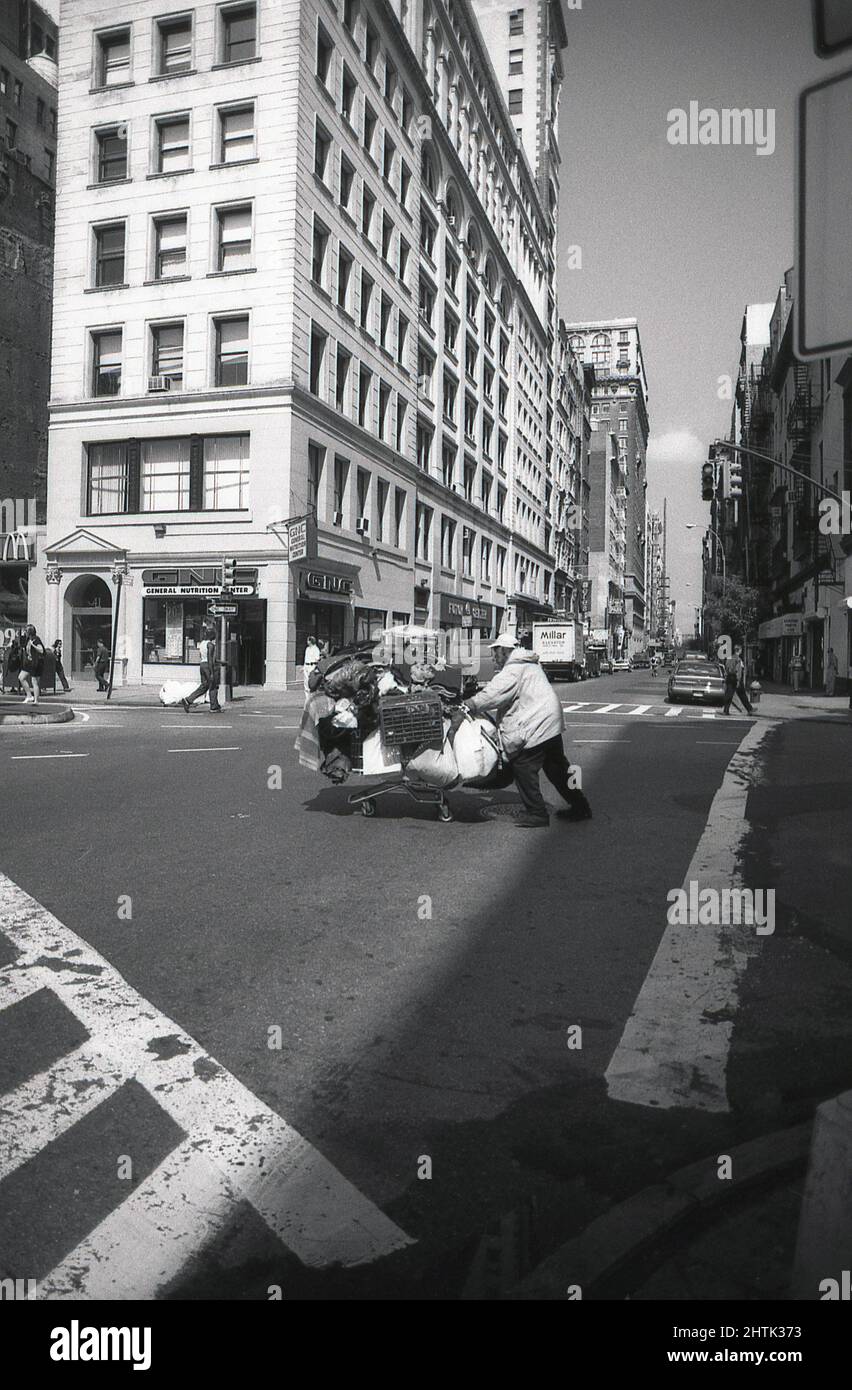 1980s, historique, un homme sans abri avec ses effets personnels chargé sur un chariot de magasinage traversant une rue de la ville, centre-ville de Manhttan New York, NY, États-Unis. Banque D'Images