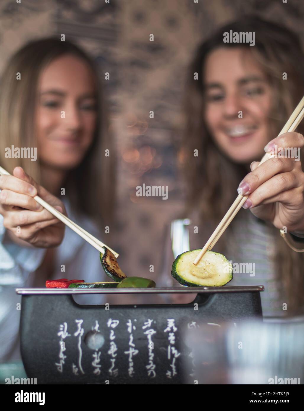 Attention sélective de deux clients heureux femme. Apprécier et manger avec des baguettes au restaurant japonais, les mains en gros plan et le fond flou. Banque D'Images