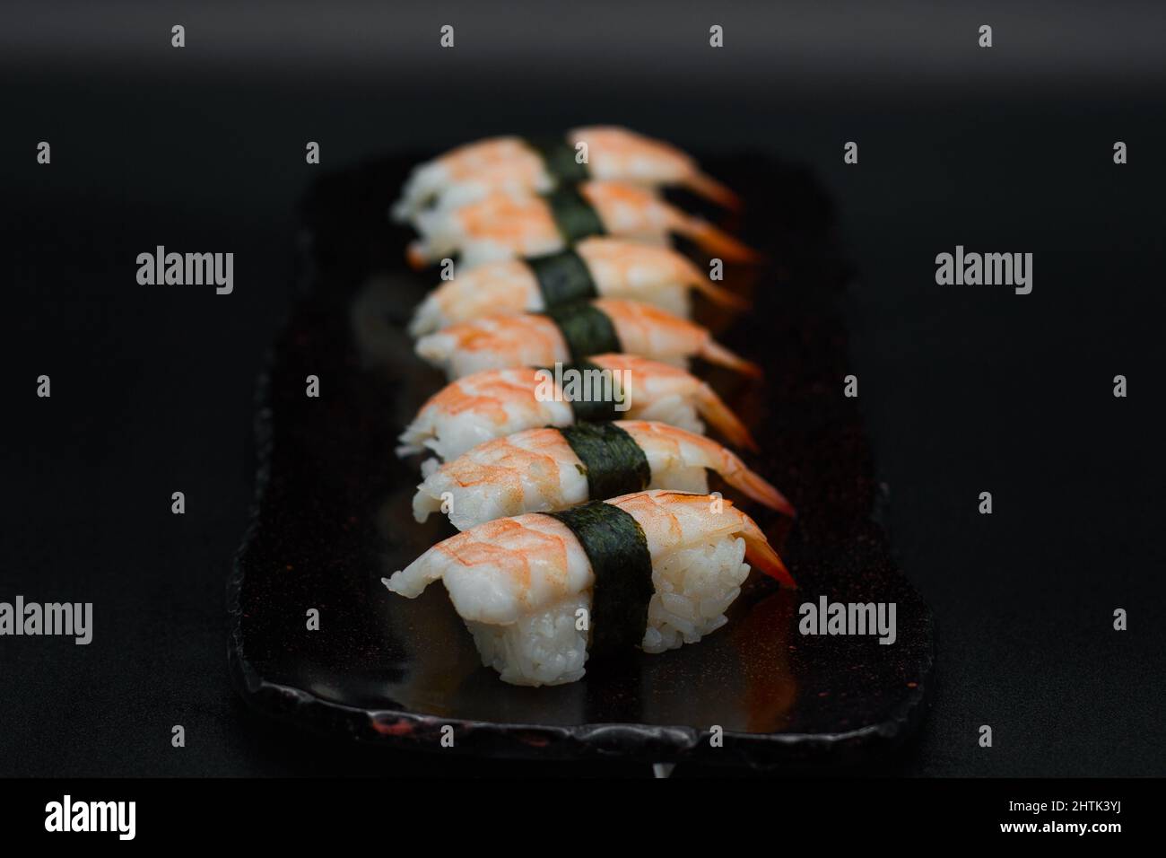 Huit unités de nigiris aux crevettes de qualité supérieure EBI King servies dans une assiette noire sur fond noir par un chef de restaurant japonais. Banque D'Images