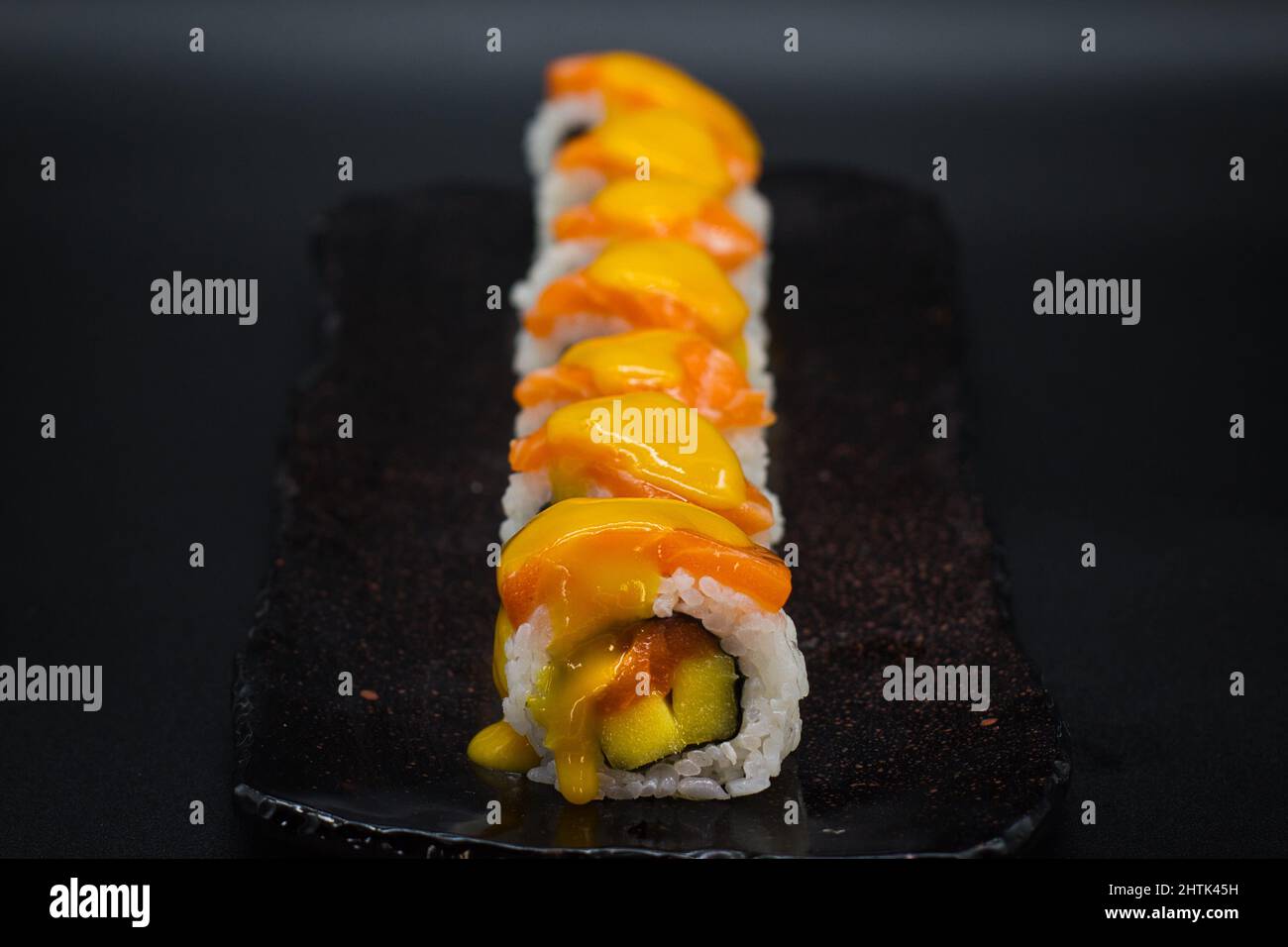 Mélange tropical de rouleaux de sushi traditionnels japonais Uramaki avec saumon sauvage, fruits frais à la mangue et sauce douce à la mangue. Arrière-plan noir. Banque D'Images