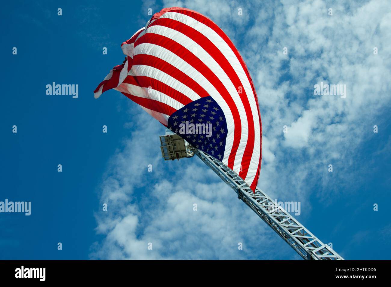 American Flag vole depuis le boom hydraulique de lutte contre les incendies. Ciel bleu au-dessus avec des nuages épars. Banque D'Images