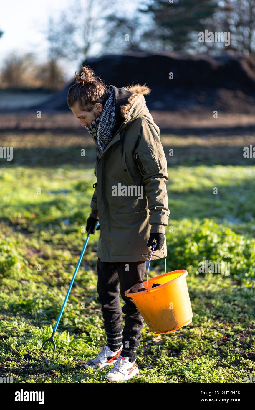 Un jeune homme avec un préparateur de litière et un seau pour recueillir la litière et les ordures de la campagne. Collecte de litière, déchets, concept environnemental Banque D'Images
