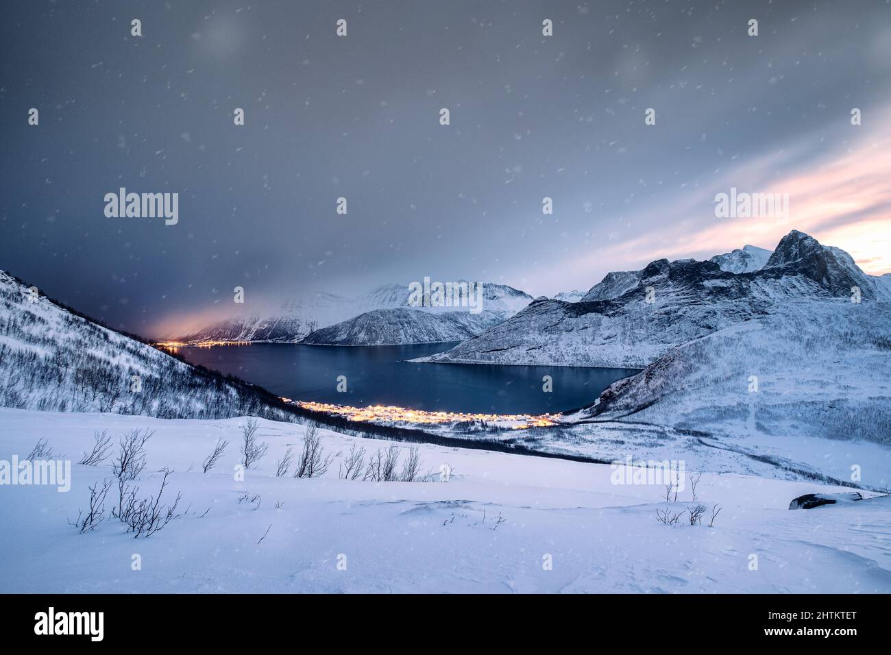 Paysage de chaîne de montagne enneigée avec ville illuminée sur la côte dans le blizzard au mont Segla, île de Senja, Norvège Banque D'Images