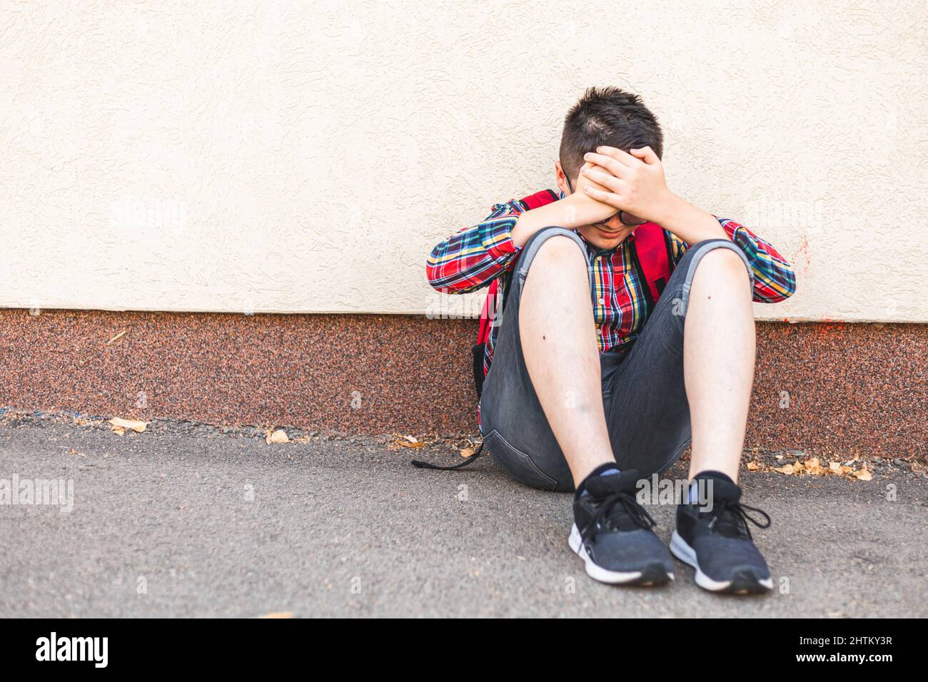 Garçon solitaire assis seul sur le sol, isolé de ses pairs, se cachant Banque D'Images