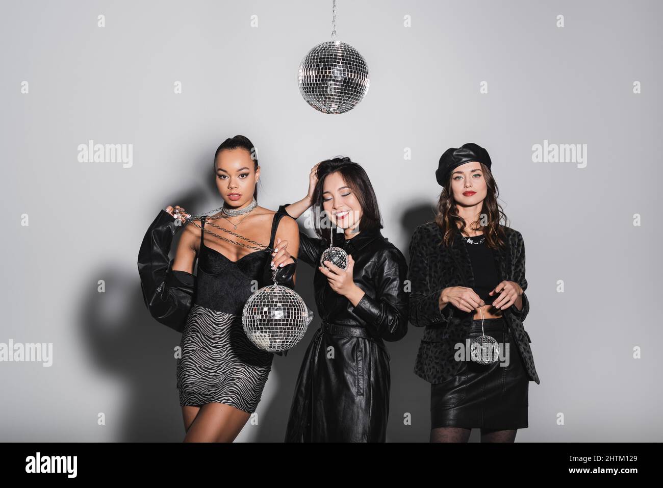 femme asiatique gaie posant près de modèles interraciaux tenant des boules disco sur le gris Banque D'Images