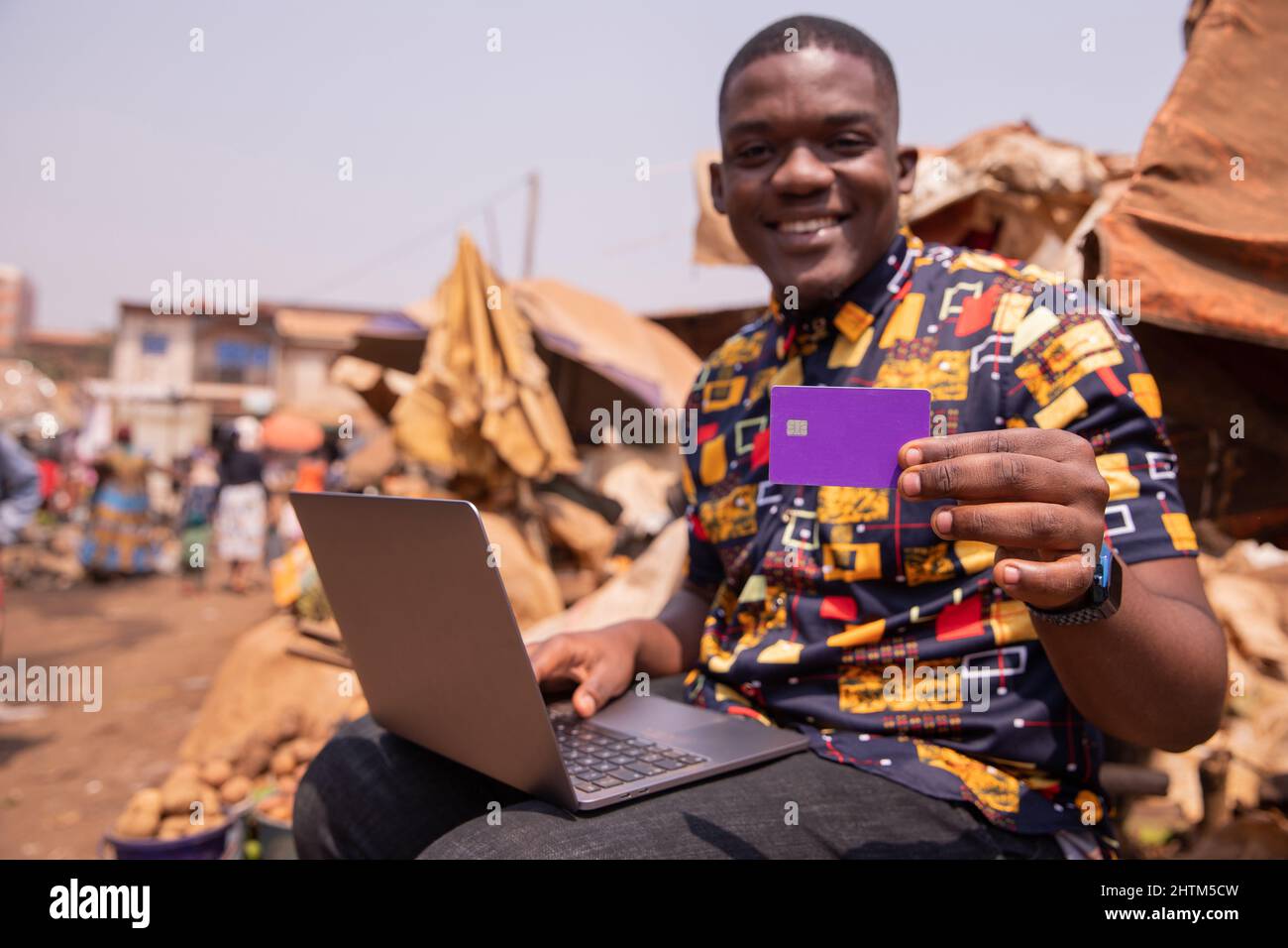 African boy montre sa carte de crédit tout en utilisant son ordinateur portable, il est sur le marché. Paiement par carte de crédit en Afrique concept Banque D'Images