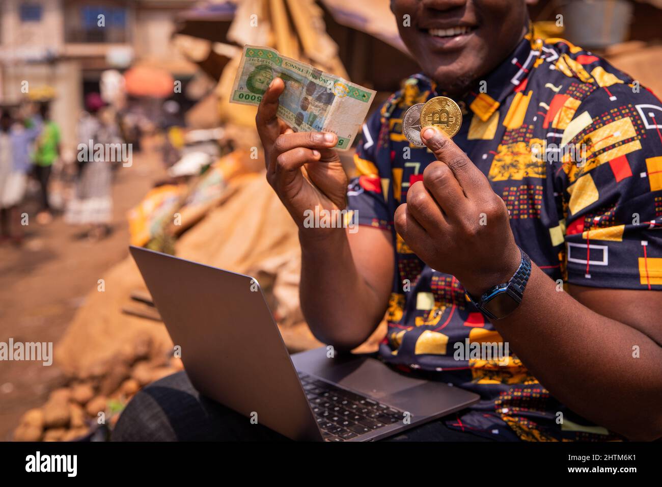 Gros plan des mains d'un garçon africain tenant une pièce de Bitcoin et d'Ethereum et une note de 5000 franc CFA. Paiements numériques en Afrique concept Banque D'Images