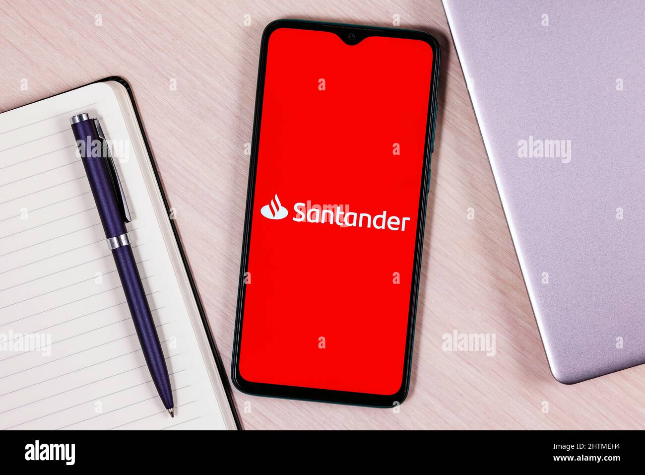 Smartphone avec logo de banque Santander sur une table en bois à côté de l'ordinateur portable et du planificateur d'affaires Banque D'Images