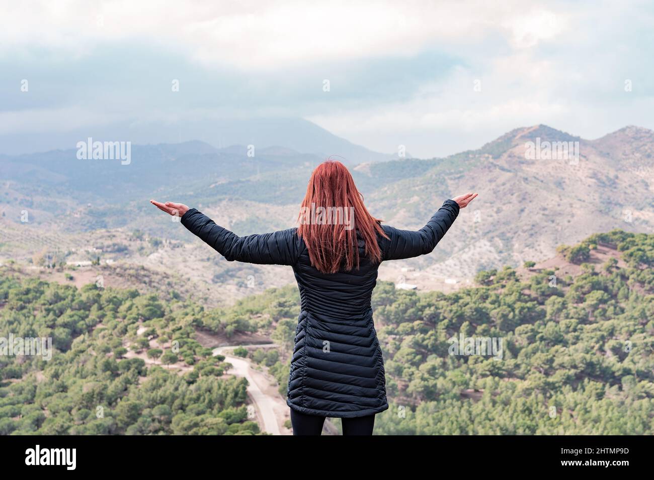 une femme aux cheveux rouges à bras ouverts regarde un horizon montagneux Banque D'Images