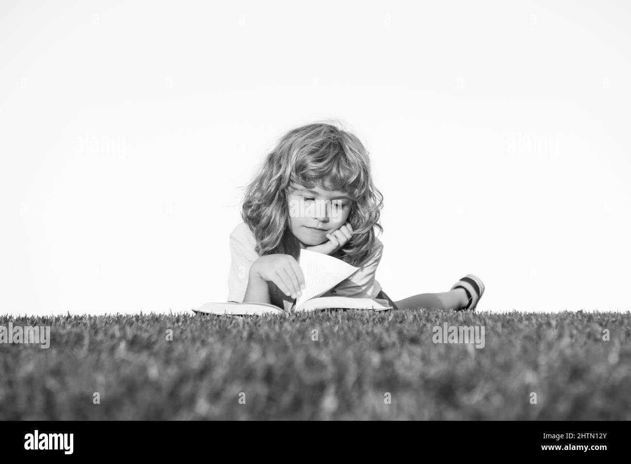Livre de lecture intelligent pour enfants, posé sur l'herbe dans le champ sur le ciel et le champ d'herbe. Portrait des enfants intelligents. Banque D'Images