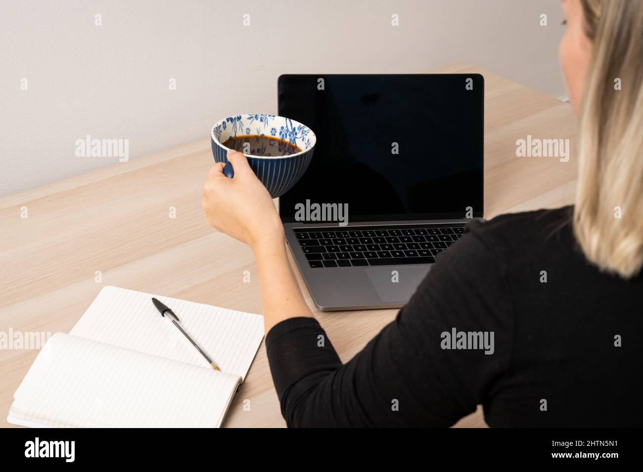 Gros plan d'une femme tenant une tasse à café au bureau avec ordinateur portable et bloc-notes Banque D'Images Gros plan d'une femme tenant une tasse à café au bureau avec ordinateur portable et bloc-notes Banque D'Images