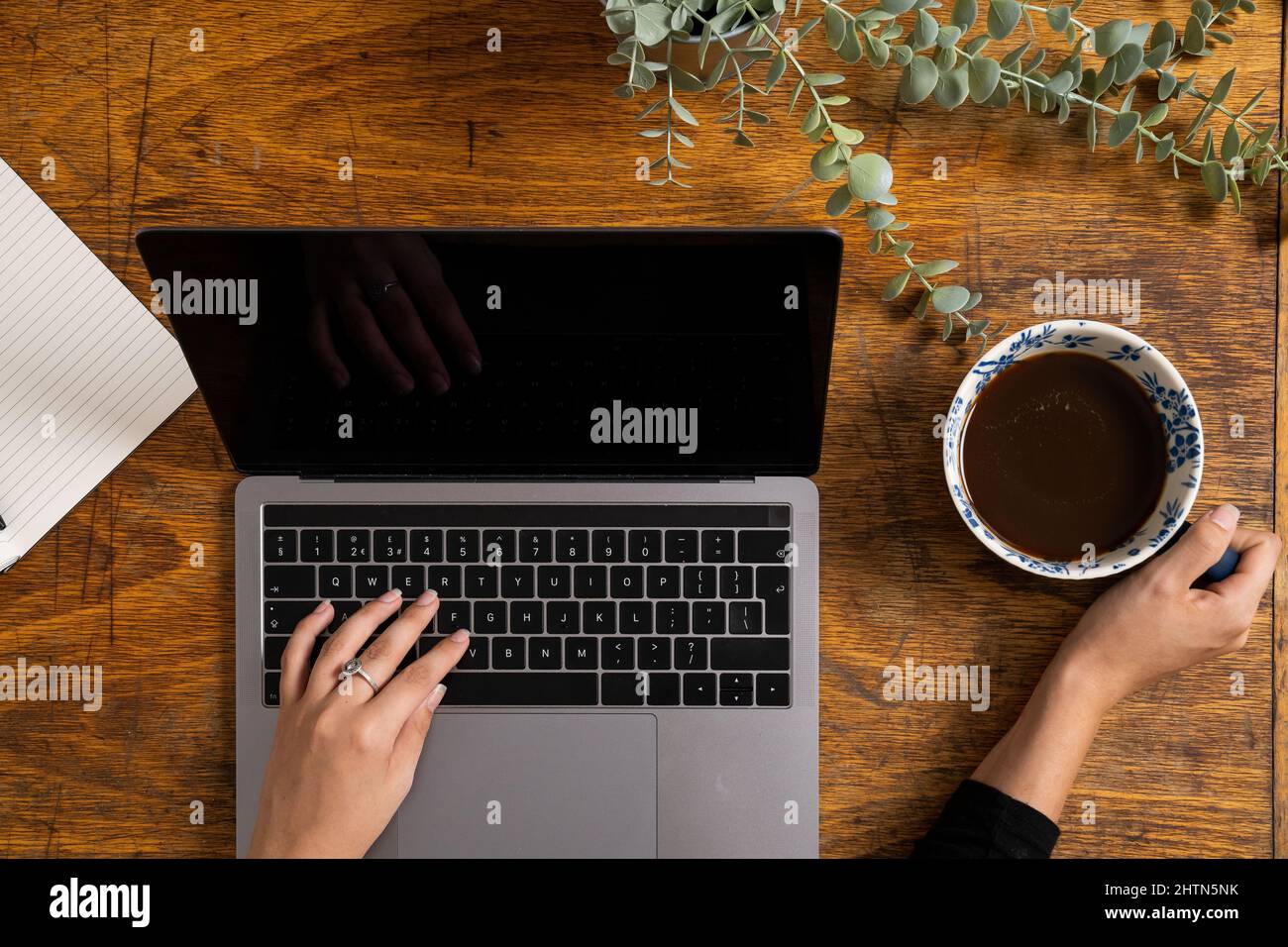 Vue de dessus des mains d'une femme qui tape sur un ordinateur portable et tient une tasse à café Banque D'Images Vue de dessus des mains d'une femme qui tape sur un ordinateur portable et tient une tasse à café Banque D'Images