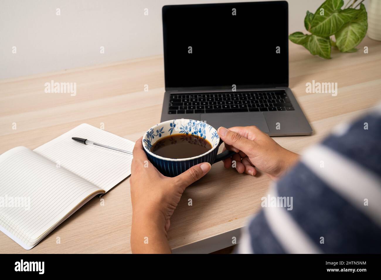 Gros plan des mains d'une femme tenant une tasse de café au bureau avec ordinateur portable et bloc-notes Banque D'Images Gros plan des mains d'une femme tenant une tasse de café au bureau avec ordinateur portable et bloc-notes Banque D'Images