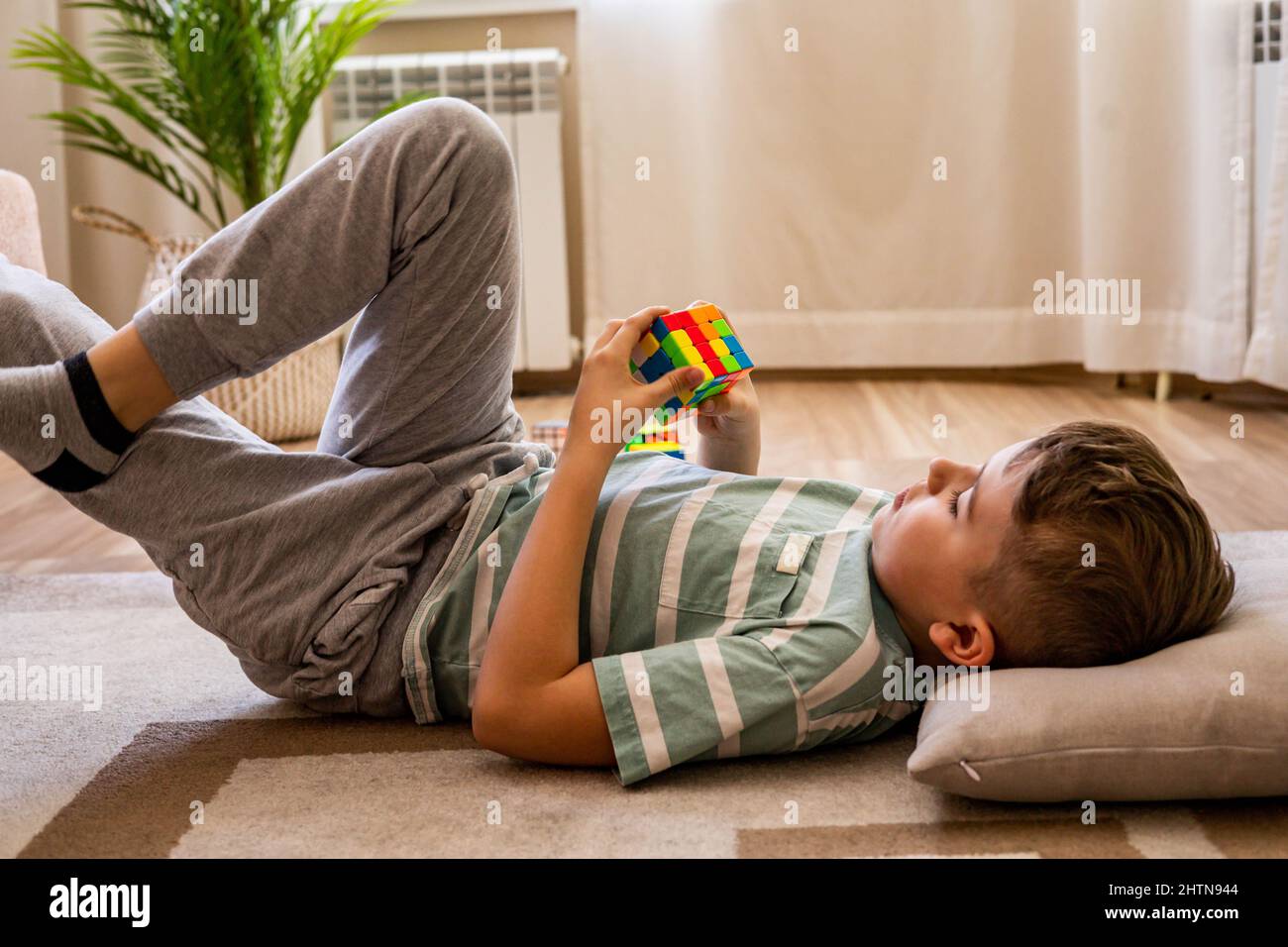 Garçon adolescent décontracté couché sur un plancher en bois assemblant le  cube de Rubik 4x4 résoudre la décision logique Photo Stock - Alamy