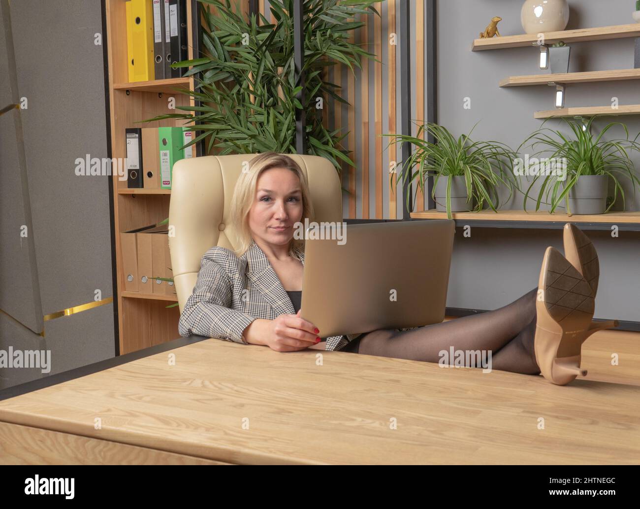 Les pieds sur la table sur un blond d'ordinateur portable dans une veste d'affaires fille ordinateur portable jeune, de la personne caucasienne de la maison de style de vie en utilisant, étude hispanique Banque D'Images