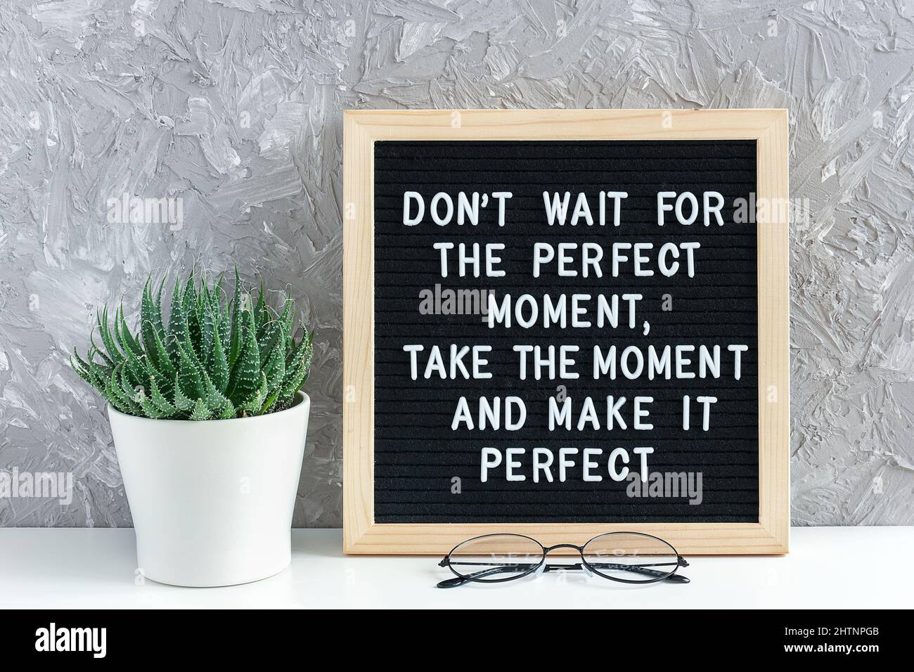 N'attendez pas le moment parfait, prenez le moment et rendez-le parfait. Citation motivationnelle sur le tableau de lettres, fleurs succulentes et verres sur la table. Con Banque D'Images