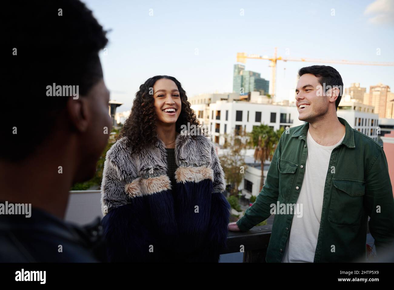 Une femme biraciale discutant avec un groupe d'amis multiculturels en train de se rencontrer sur une terrasse sur le toit au crépuscule. Banque D'Images