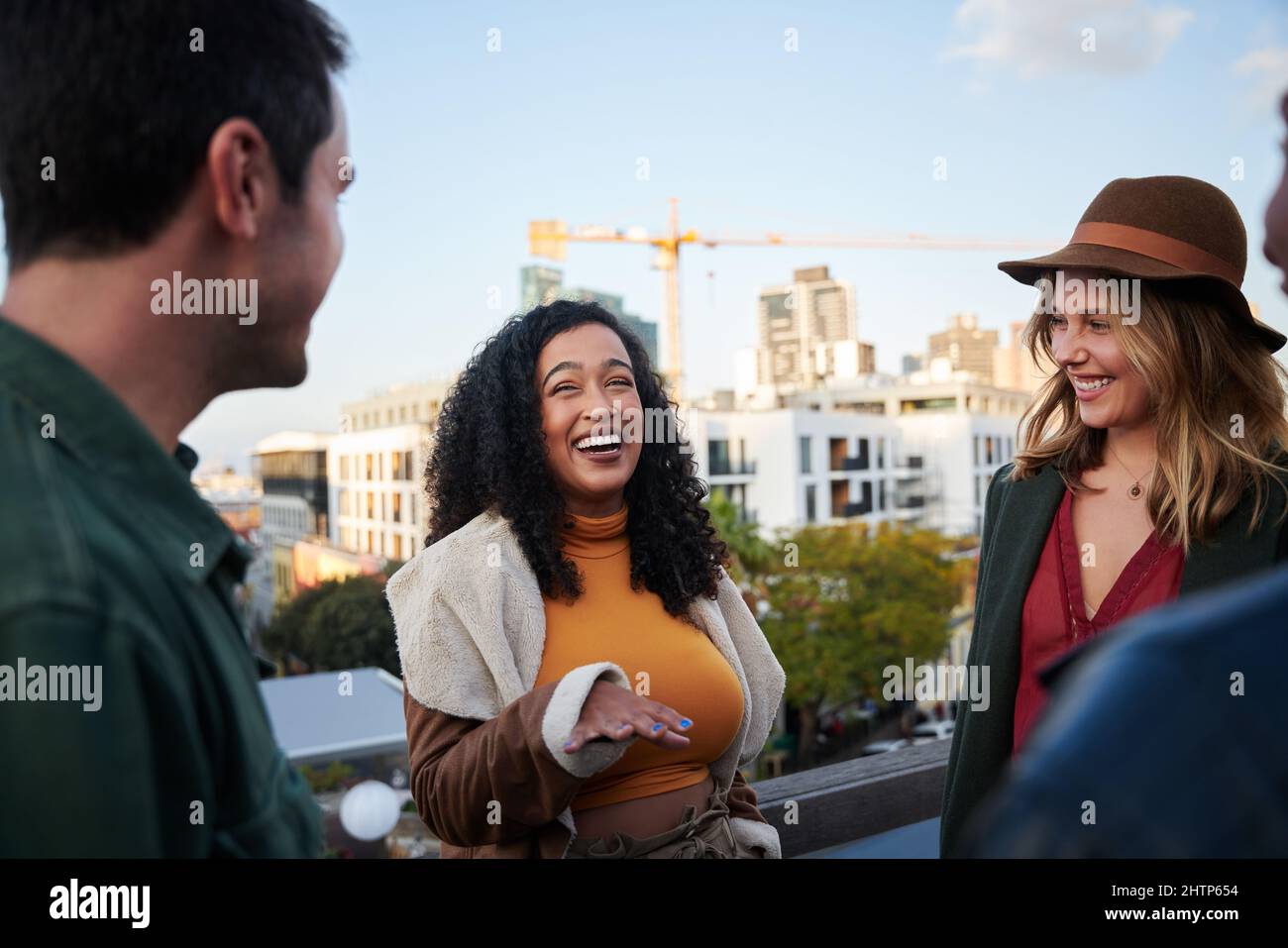 Une femme biraciale riant avec un groupe d'amis multiculturels en train de rencontrer sur une terrasse sur le toit au crépuscule. Banque D'Images