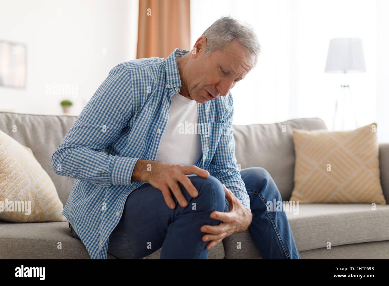 Homme mûr avec des douleurs au genou assis sur le canapé à la maison Banque D'Images