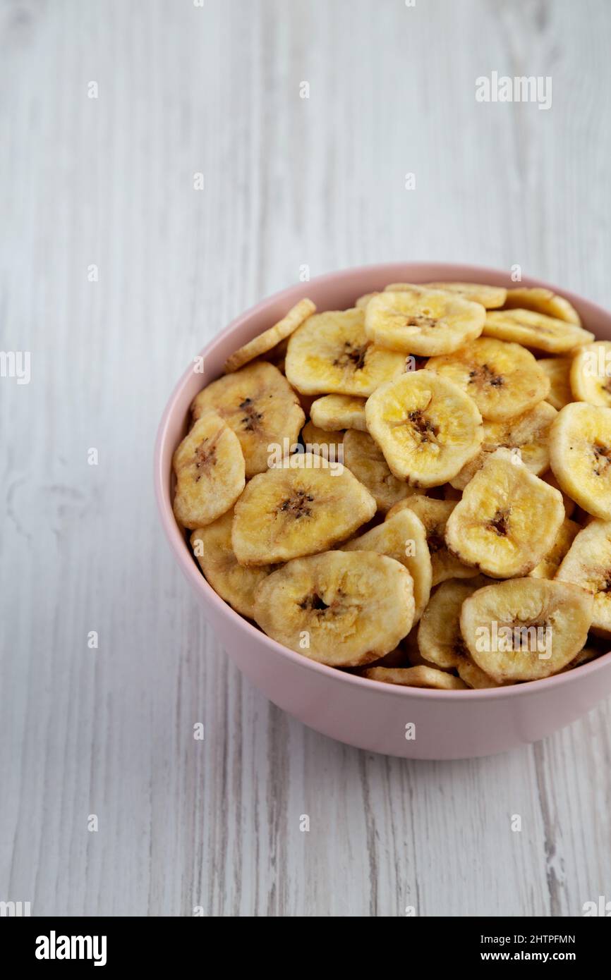 Croustilles Banana faites maison dans un bol rose sur fond de bois blanc, vue latérale. Banque D'Images