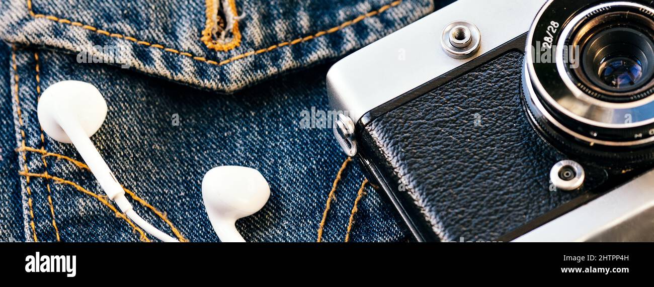 L'appareil photo et le casque avec fil blanc reposent sur l'arrière-plan du denim. Arrière-plan tendance des vêtements taille basse. Style rétro. Journée des photographes. Vue de dessus Banque D'Images
