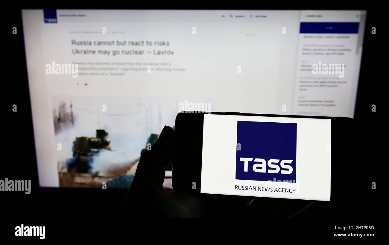Personne tenant un smartphone avec le logo de l'agence de presse russe TASS (TACC) à l'écran devant le site Web. Mise au point sur l'affichage du téléphone. Banque D'Images