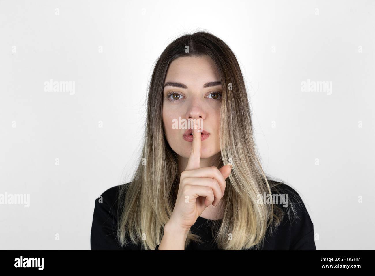 Fille montrant le geste de silence sur fond blanc. Top secret ! Ne dites à personne! Demander à être calme avec le doigt sur les lèvres pointant avec la main. Banque D'Images