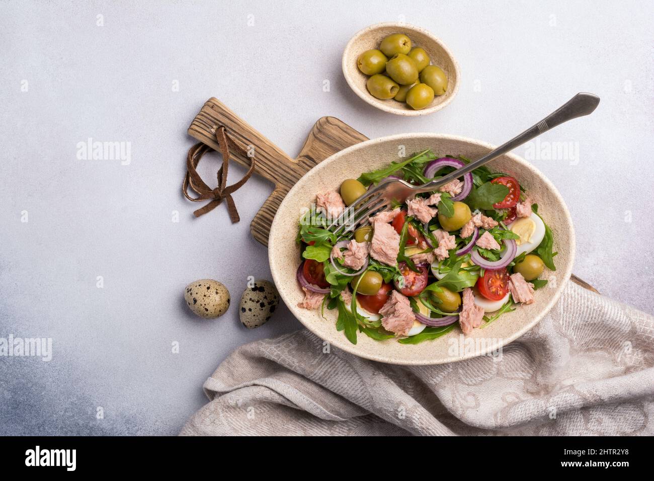 Vue de dessus de salade saine et savoureuse avec thon, arugula fraîche, tomates cerises, œuf de caille, oignon et olives vertes sur fond de béton gris Banque D'Images