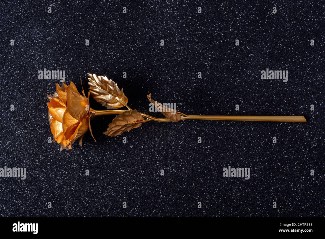 Belle fleur de rose dorée métallique faite à la main avec feuilles et tige sur fond noir avec bokeh brillant, gros plan. Décor artisanal élégant et tendance. b Banque D'Images