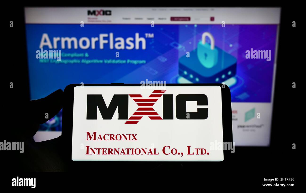 Personne tenant un téléphone portable avec le logo de la société taïwanaise Macronix International Co. Ltd. À l'écran en face de la page Web. Mise au point sur l'affichage du téléphone. Banque D'Images