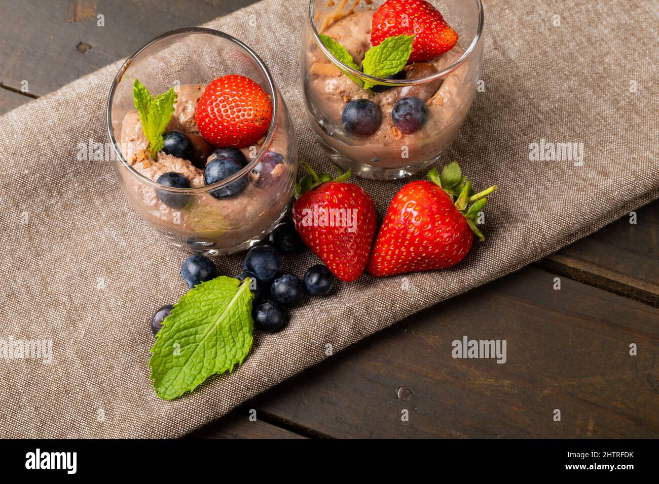 Mousse au chocolat en gros plan avec fruits aux baies, noix enrobées et feuilles de menthe servies dans des verres en toile de jute Banque D'Images