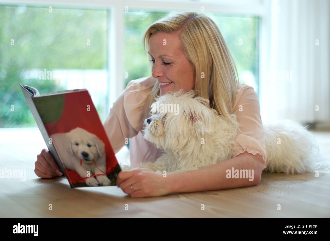 Tout savoir sur vous. Une jeune femme lisant un livre sur les chiens tout en câlinant son chien. Banque D'Images