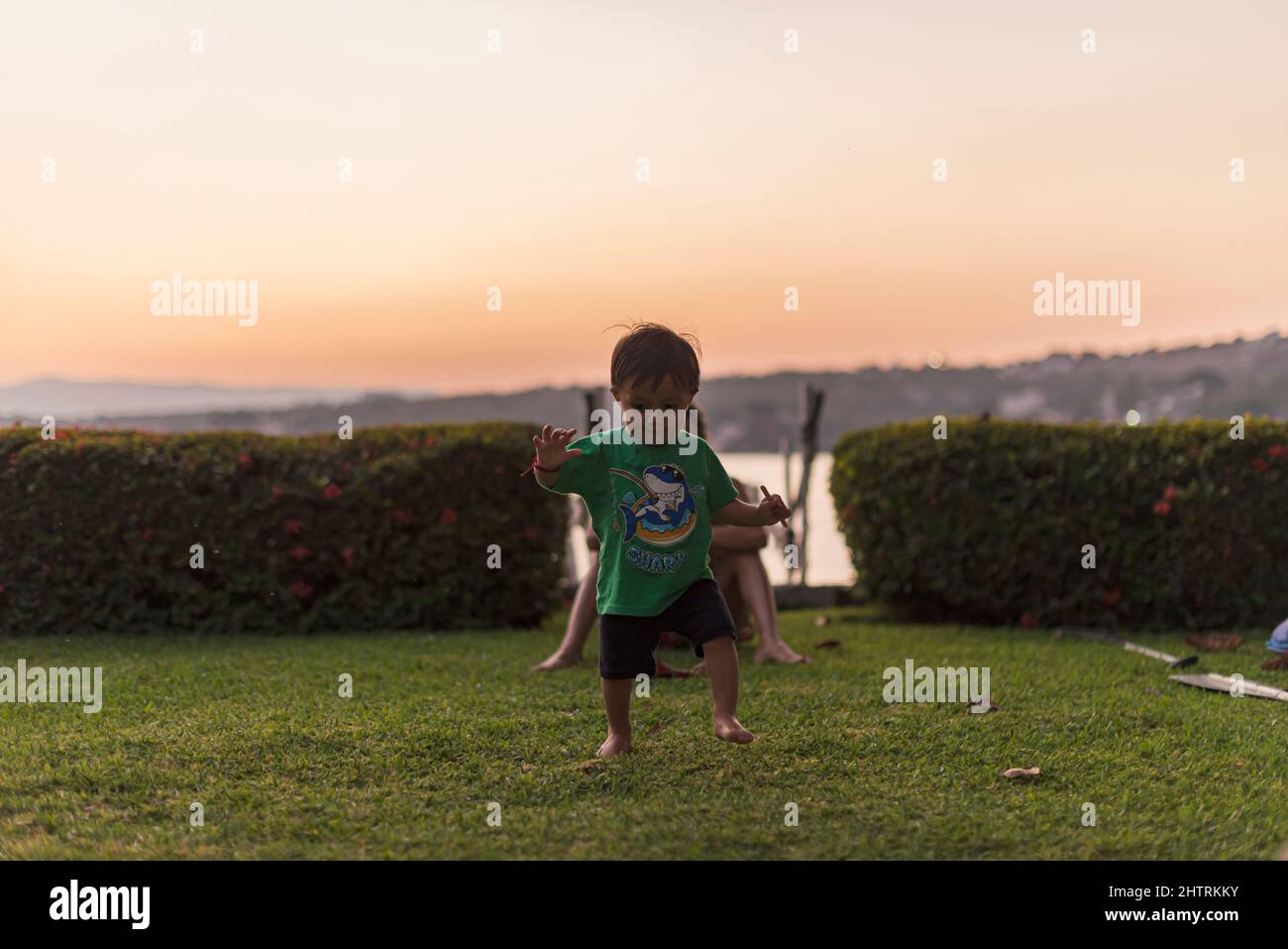 Un tout-petit adorable qui apprend à marcher dans le jardin au crépuscule Banque D'Images