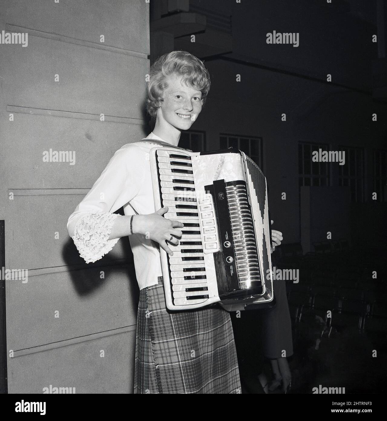 1960s, historique, une jeune écossaise en jupe tartan debout jouant un accordéon, un instrument de musique à main en forme de boîte où les touches et/ou les boutons sont pressés tout en déplaçant les deux côtés ensemble, Fife, Écosse, Royaume-Uni. Son instrument est un accordéon Paramount, il s'agissait d'une société italienne, Accordons di Eraldo & Elio Busilacchio, de Castelfidardo, qui était active de 1946 à 1982. Banque D'Images