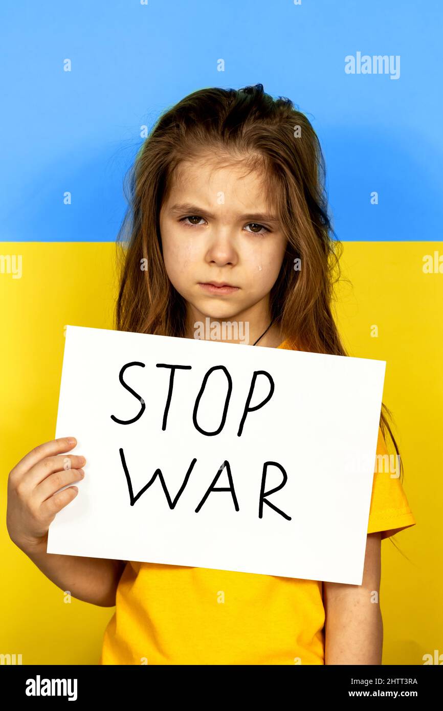 Une fille pleure, tenant une AFFICHE D'ARRÊT sur le fond du drapeau ukrainien. Arrêter la guerre en Ukraine. Le concept de paix en Ukraine. Banque D'Images