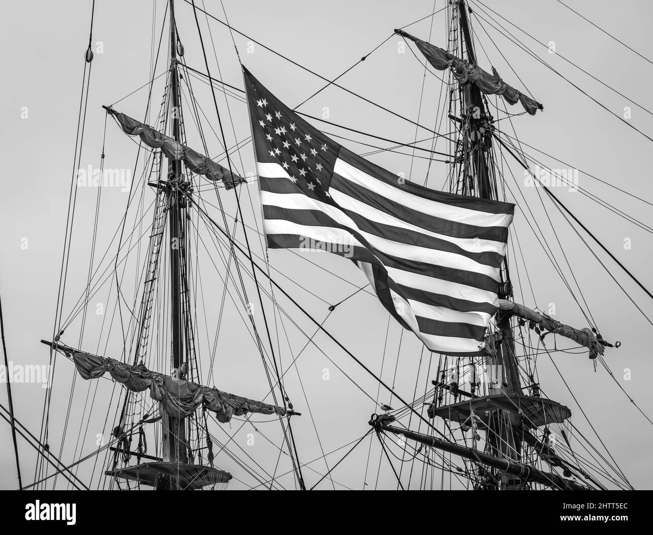 Le drapeau national américain vole de grands navires qui gréent avec des mâts d'un autre grand navire en arrière-plan. Banque D'Images