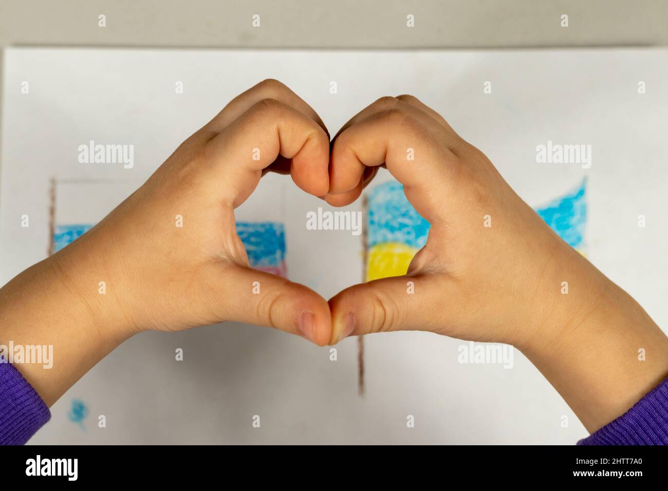 Un enfant fait un signe de coeur avec ses mains sur un dessin de deux drapeaux de l'Ukraine et de la Russie gros plan. Vue de dessus. Les enfants contre la guerre. Banque D'Images