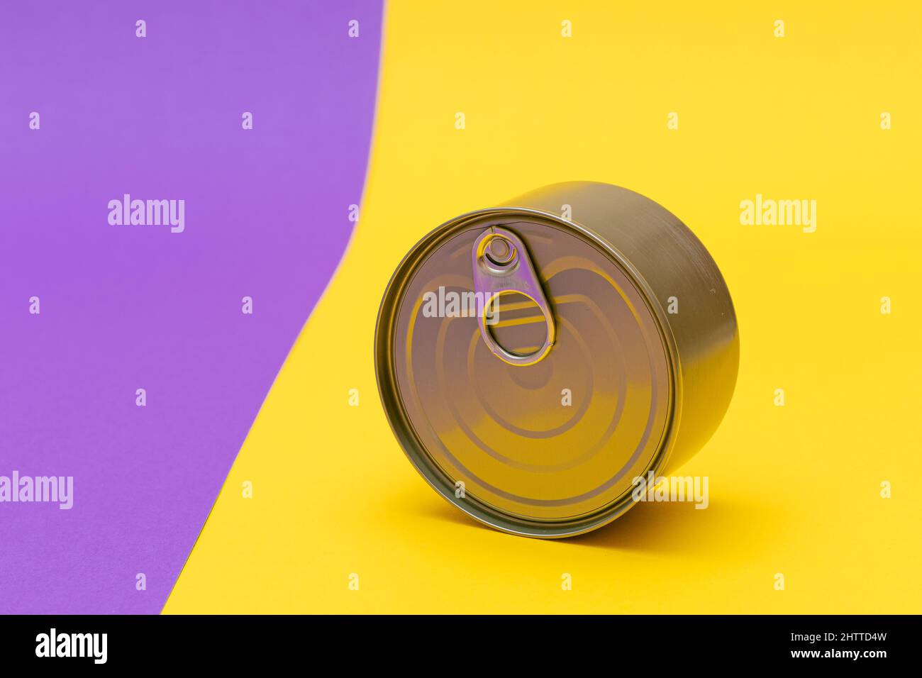 Boîte en étain non ouverte avec bord vierge sur fond jaune fendu et violet.Aliments en conserve.Boîte en aluminium pour un stockage sûr et à long terme des aliments.Conteneur d'entreposage des aliments scellé en acier Banque D'Images