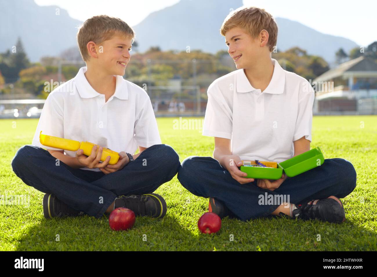 Qu'avez-vous pour le déjeuner ? Deux jeunes écoliers assis sur l'herbe sur le point de manger leur déjeuner. Banque D'Images