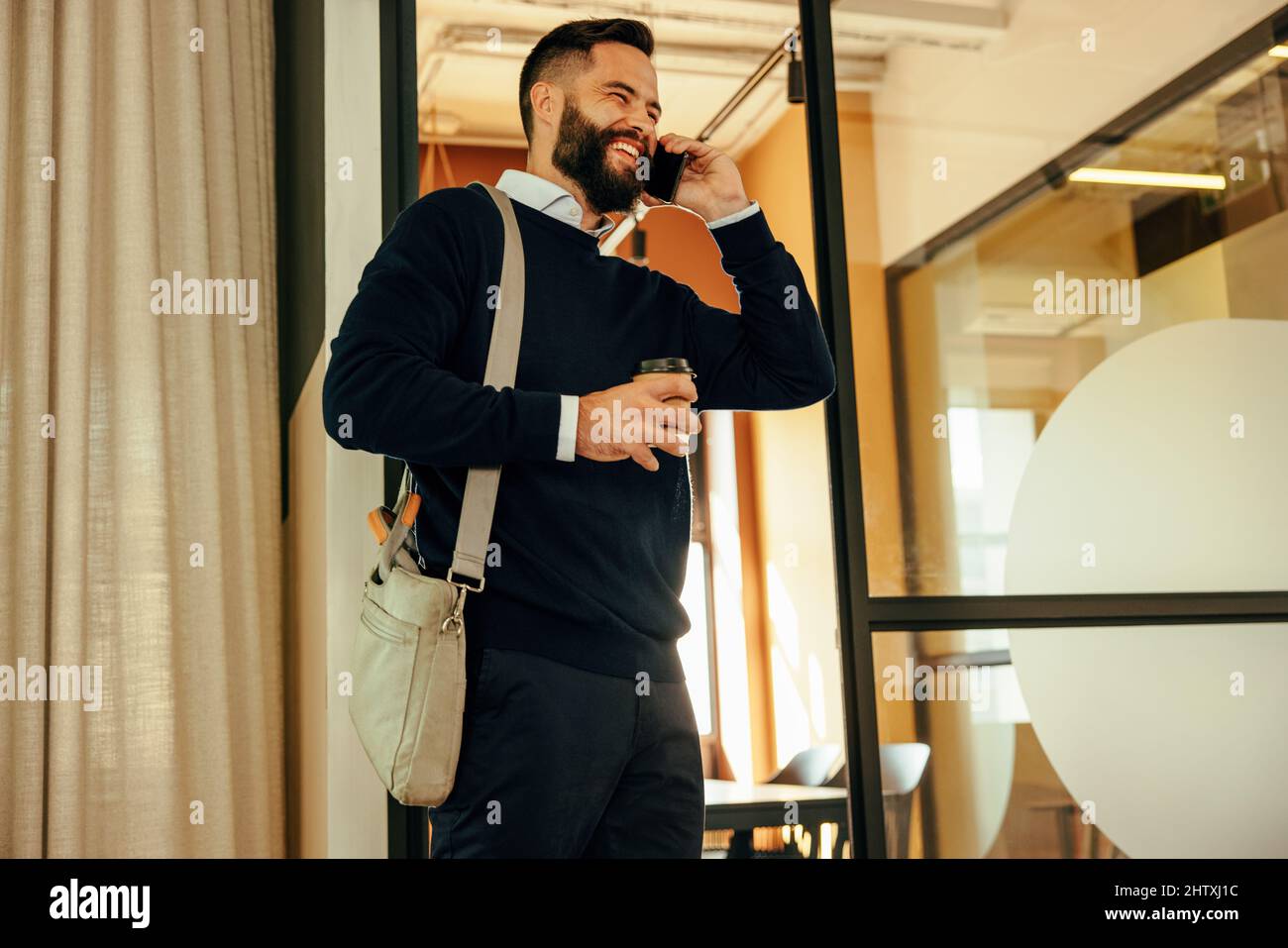 Joyeux homme d'affaires souriant en parlant au téléphone le matin. Un jeune homme d'affaires souriant communique avec ses collaborateurs après arri Banque D'Images