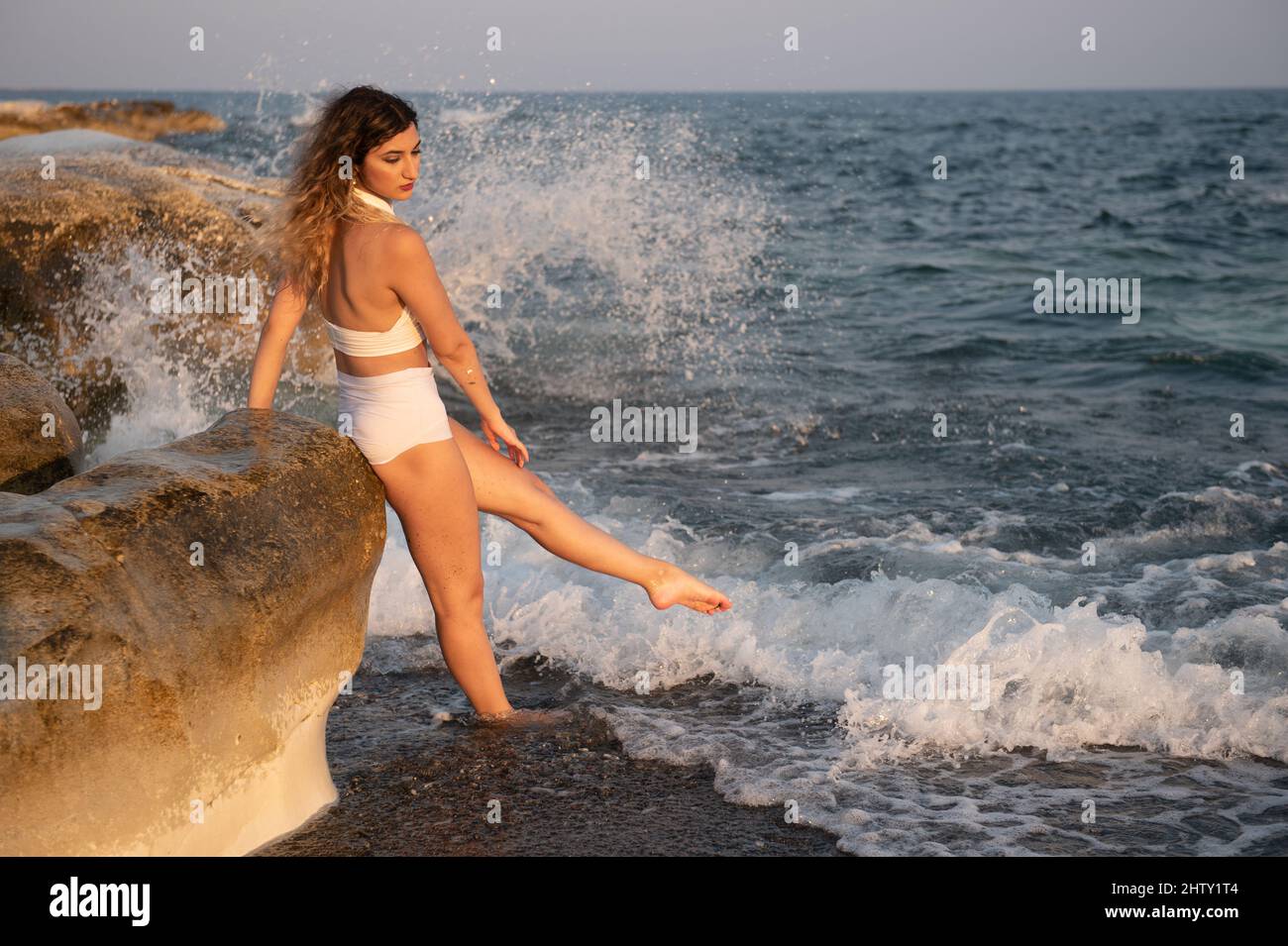 Jeune femme portant un maillot de bain blanc jouant dans l'eau à la plage.  Coucher de soleil sur la mer Photo Stock - Alamy