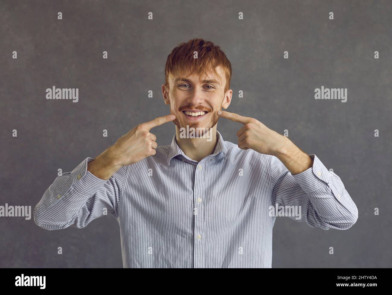 Jeune homme portant une chemise décontractée montrant des dents blanches sur fond gris Banque D'Images