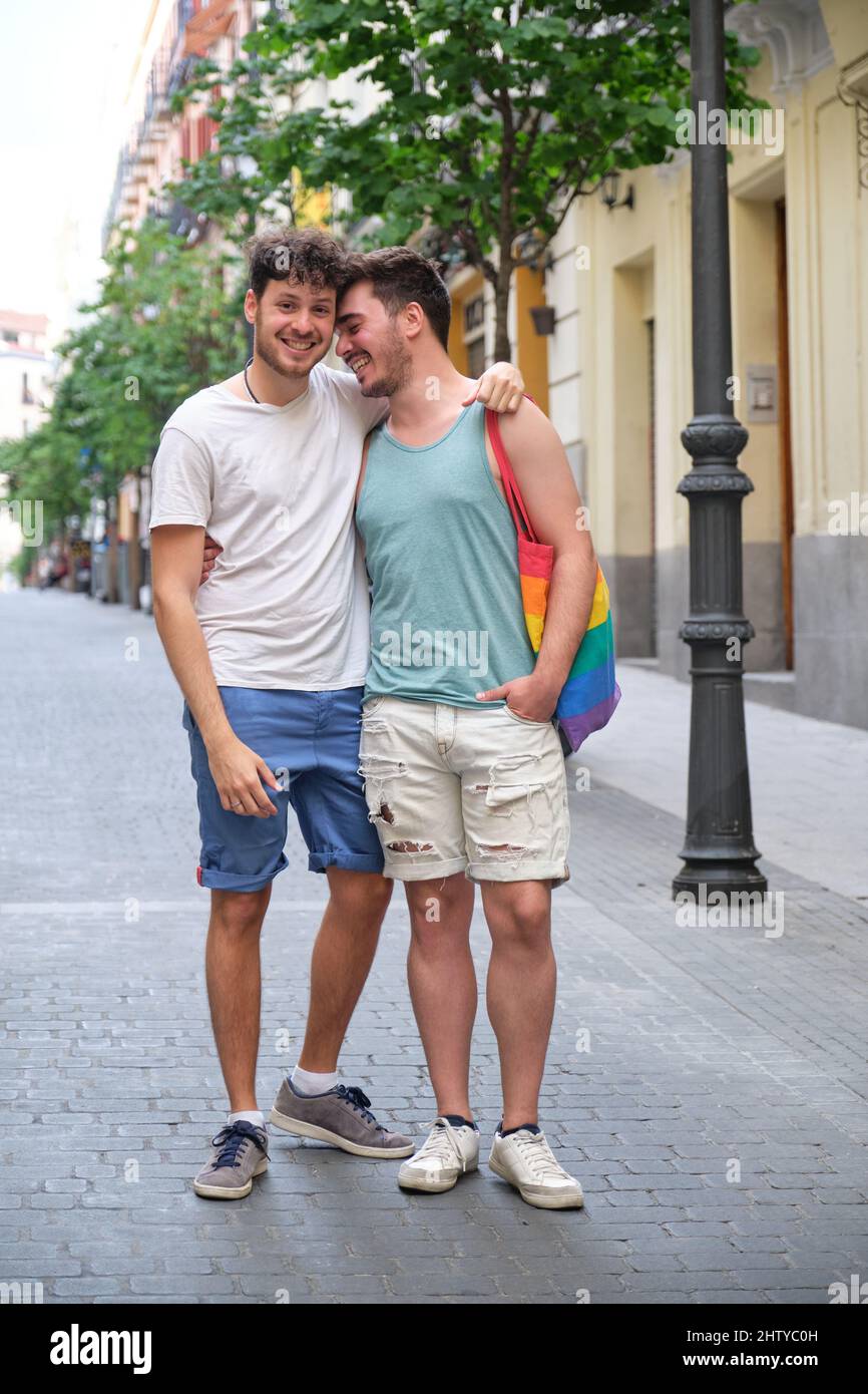 Un couple gay riant en train de se serrer et de regarder un appareil photo dans la rue. Banque D'Images