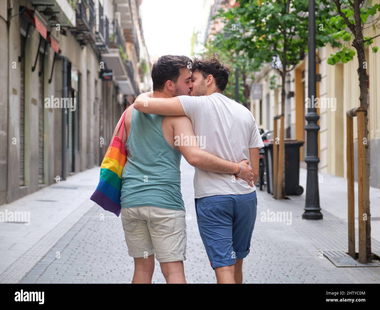 Un couple gay riant et embrassant assis sur un banc tenant des drapeaux LGBT. Banque D'Images