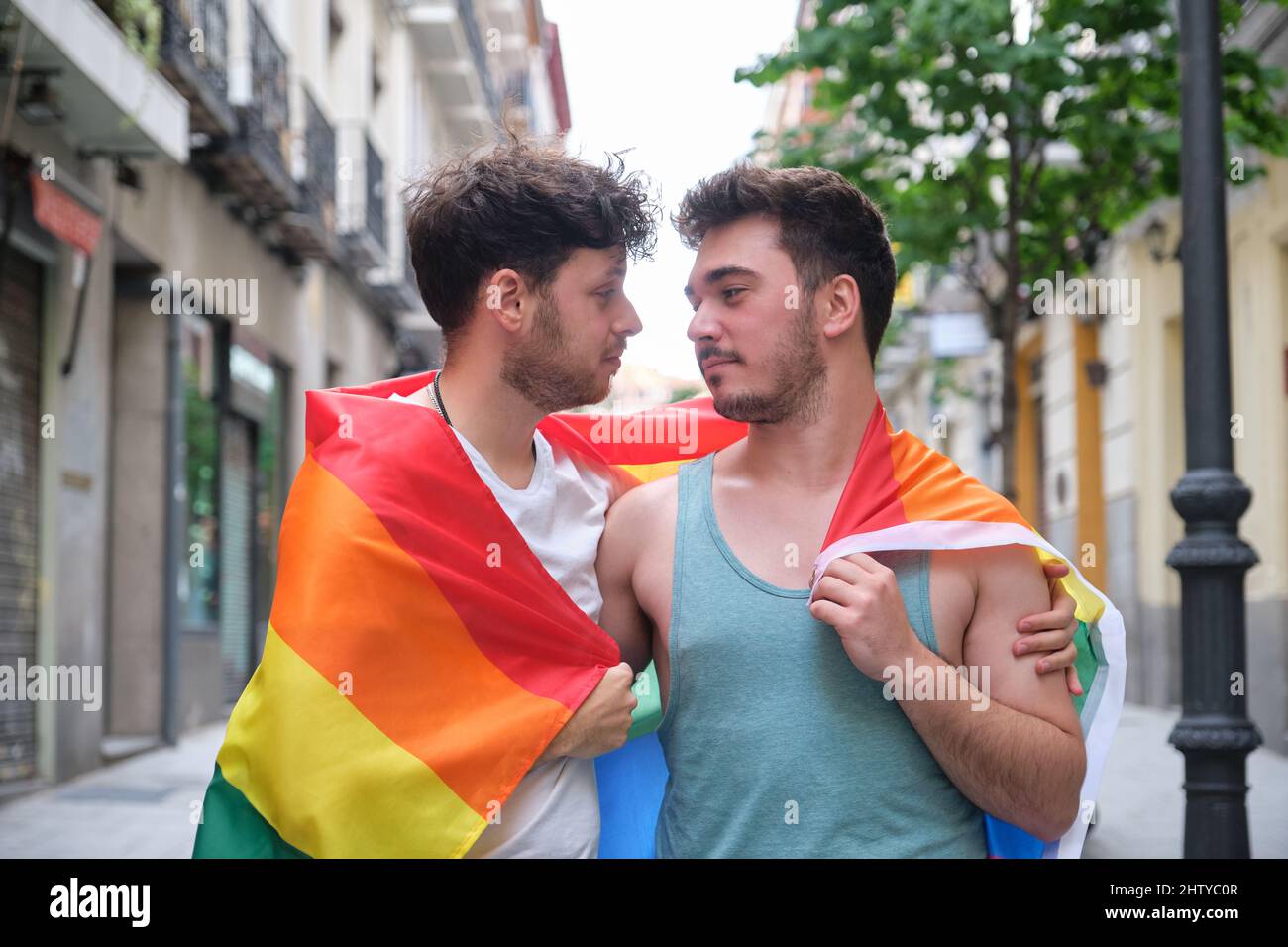Un couple gay s'est enveloppé dans un drapeau LGBT, s'embrassant et regardant l'un l'autre. Banque D'Images
